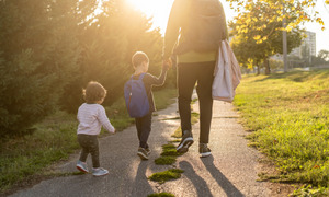 A parent walking with their two children on a path outdoors.