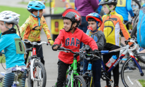 A group of children around 8 years old are on bicycles together, the child in the middle of the picture wears a helmet with a red mohawk down the centre.