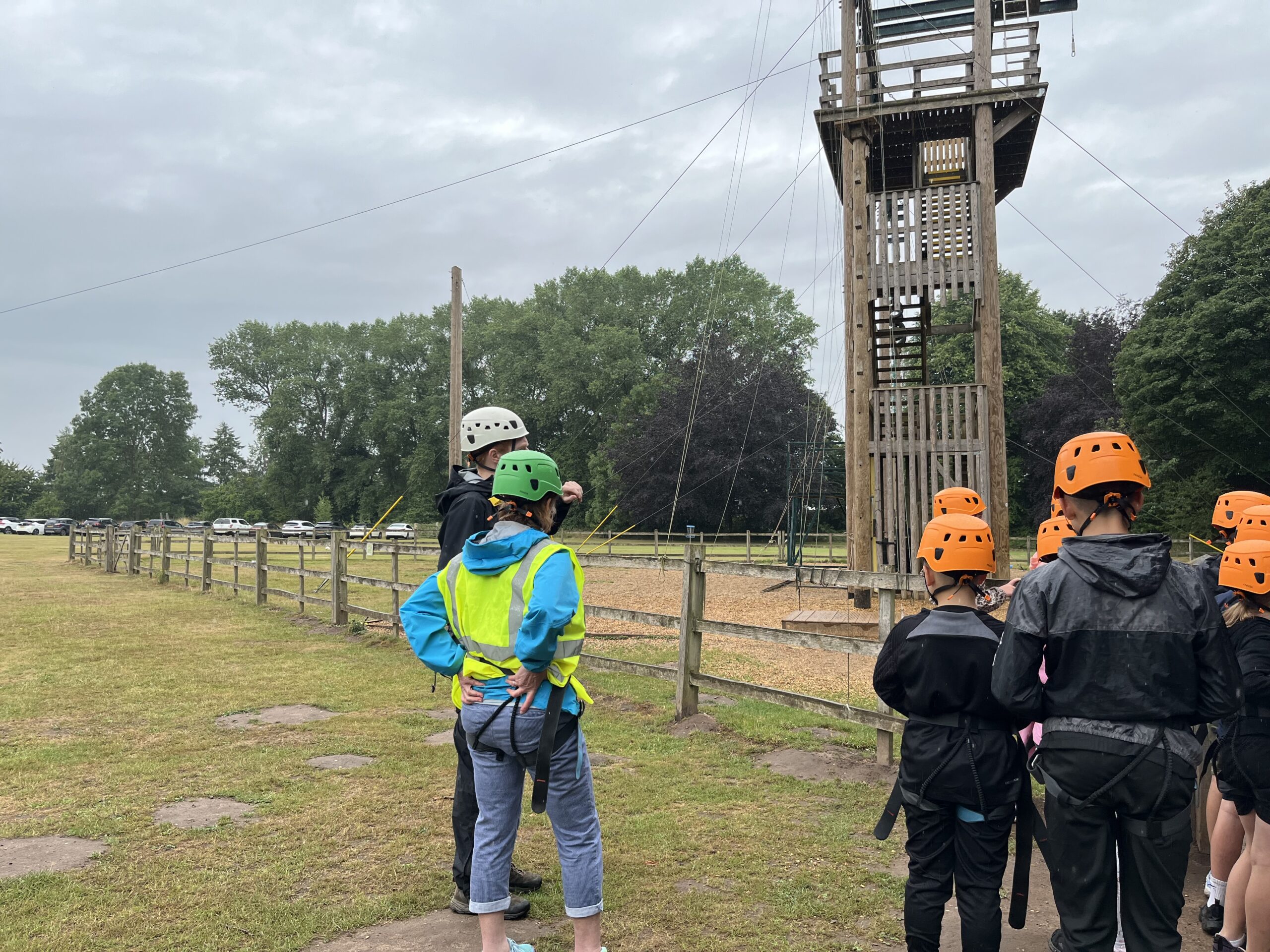 Image shows children and an instructors looking up at a wood framed climbing structure for an outdoor activity.