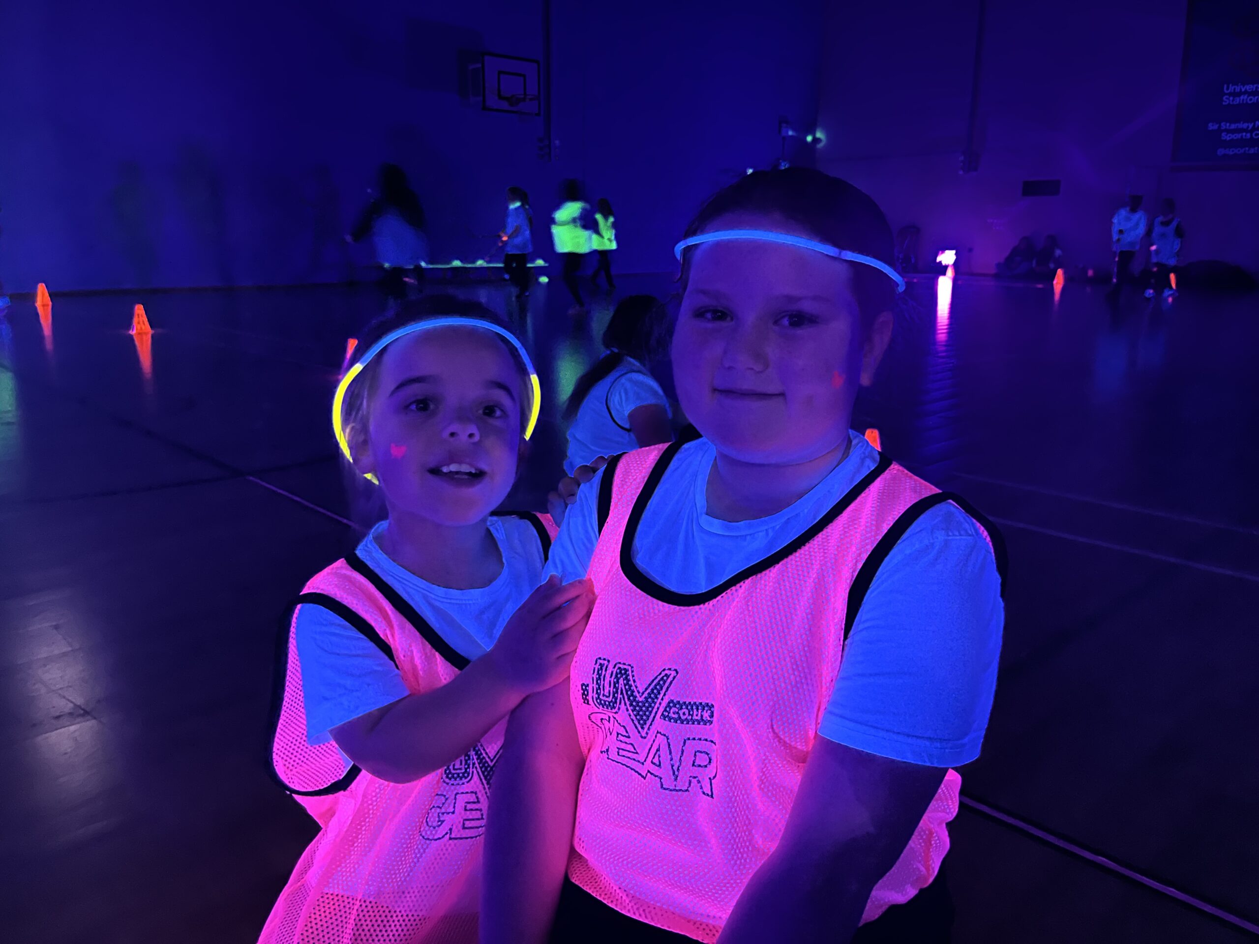 Image shows a two young girls in glow in the dark jerseys. Image is taken in a dark sports hall as part of a glow in the dark sport event.